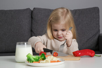 Portrait of adorable toddler girl preparing healthy meal, cutting vegetable with knife.