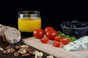 Cherry tomatoes, Olives, Blue cheese, Homemade bread, Walnuts, Almonds and Orange juice on wooden table on a dark background.