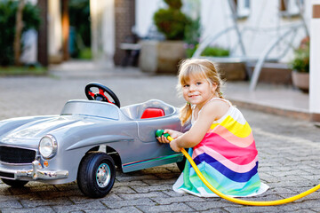 Little toddler girl playing with big vintage toy car and having fun outdoors in summer. Cute child...