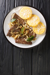 Fried beef liver with onion and sage, served with polenta close-up in a plate on the table. vertical top view from above