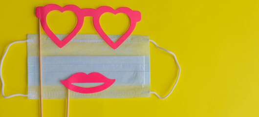 Medical face mask, paper glasses and pink lips on stick on bright yellow background, close-up. April Fools ' Day during coronavirus pandemic concept. Copy space.