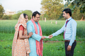 Fototapeta na wymiar Young rural indian couple farmer receive money from banker at agriculture field.