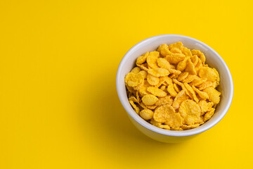cornflakes are poured into a bowl on a yellow background