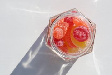 Sweet fruit hard candies in the glass mason jar on white table background. Overhead view of...