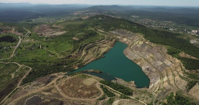 Inoperative blue water flooded quarry with big dumps. Mining industry in Ural Mountains. Aerial drone wide view at summer sunny day