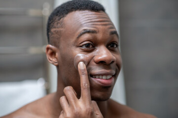 African american short-haired guy applying some cream on his face