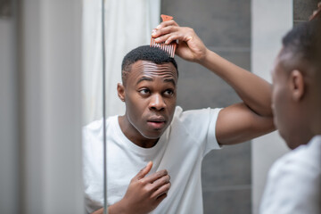 African american guy in white tshirt doing his hair in the bathroom