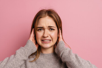 Ginger displeased woman looking at camera while covering her ears