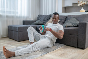 Dark-skinned young guy sitting on the floor and looking at his smartwatch