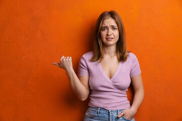 Young ginger unhappy woman grimacing while pointing finger aside