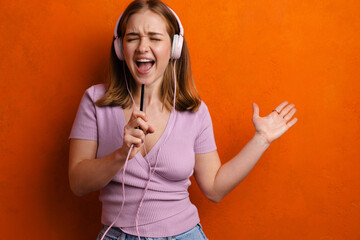 Fototapeta premium Joyful woman singing while listening music with headphones and cellphone