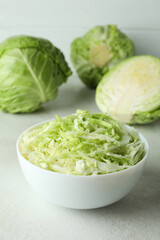 Bowl with sliced cabbage and fresh cabbage on white textured table