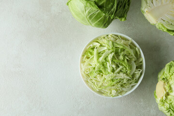 Bowl with sliced cabbage and fresh cabbage on white textured table
