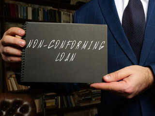 woman's hand showing black notepad with phrase NON-CONFORMING LOAN - closeup shot on grey background