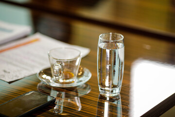 Shallow depth of field (selective focus) image with an empty coffee cup and a glass of sparkling water on the desk of a businessman during a corporate meeting.