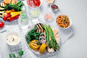 Delicious grilled vegetables with sauces and snacks served on light gray background.