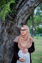 Portraiture of Happy pregnant Muslim woman caressing belly in park.