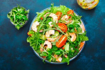 Fresh shrimp salad with tomatoes, lettuce, arugula, avocado, cucumber and lemon dressing on blue background. Healthy eating, clean food concept. Top view
