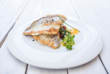 Pescado cocinado con verdura y servido en plato. Fish steak on plate with roasted vegetables. Close up on a plate