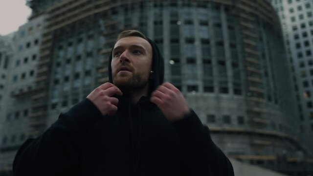 Caucasian male athlete walking through city wearing hoodie and earphones