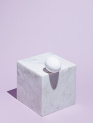 Geometric composition with marble cube and white egg on the edge against pastel violet background. Creative Easter holiday concept. Abstract isometric food layout with trend summer shadows.