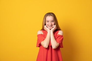 Enjoying life concept. Pleasant looking glad european girl  looks aside, has smile with braces, keeps hands together under chin, dreams about something.