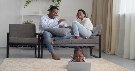 Young responsible parents african american couple sitting on couch talking speaking while little preschool girl looks at laptop screen browsing surfing net playing computer games studying remotely