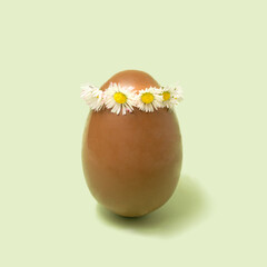 Big chocolate egg with daisy chain headpiece minimal arrangement. Mint green background.