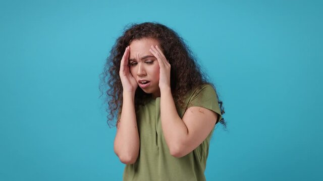 Shocked worried scared young african american woman 20s years old in green khaki t-shirt posing isolated on blue background studio. People lifestyle concept. Covering face with palms put hands on head
