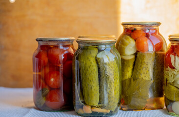 Glass jars with pickled cucumbers (pickles), pickled tomatoes and cabbage. Jars of various pickled vegetables. Canned food in a rustic composition.
