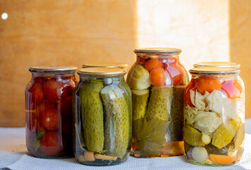 Glass jars with pickled cucumbers (pickles), pickled tomatoes and cabbage. Jars of various pickled vegetables. Canned food in a rustic composition.