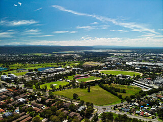 Angled aerial photograph of green grassed area amongst suburban houses on sunny summer day with blue sky