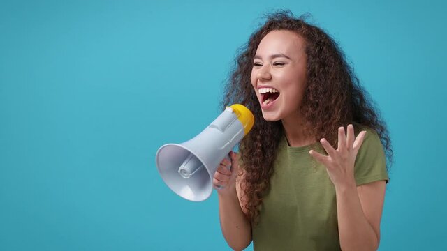 Excited funny african american woman 20s in green t-shirt posing isolated on blue background studio. People lifestyle concept. Looking aside screaming in megaphone clenching fists spreading hands
