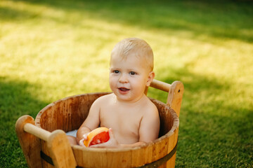 baby splashes in a basin in nature on a green tvava, at sunset. Good mood, child's smile, happiness from swimming in water, water splashes fly, good summer day