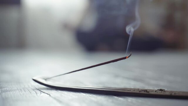 Meditation concept. Steaming incense stick close-up on the floor and yogi in the background