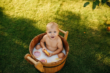 baby splashes in a basin in nature on a green tvava, at sunset. Good mood, child's smile, happiness from swimming in water, water splashes fly, good summer day