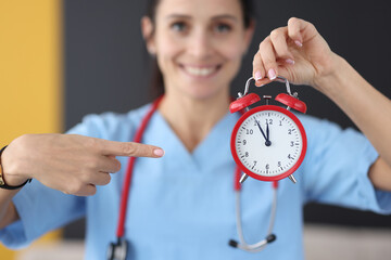 Smiling nurse points finger at red alarm clock