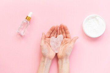 Gua sha in female hands on a pink background. Horizontal orientation, top view.