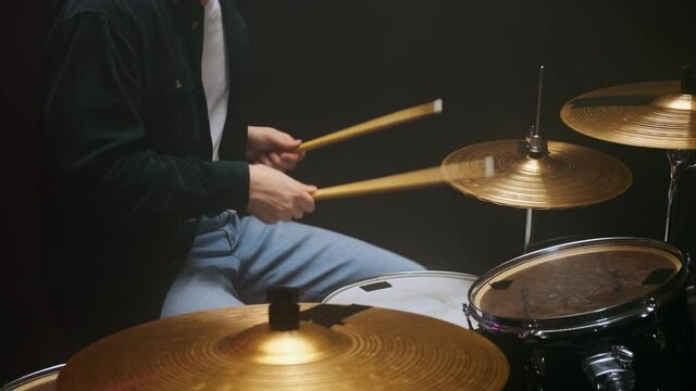 Drummer playing the drum set in a dark room on a black background.