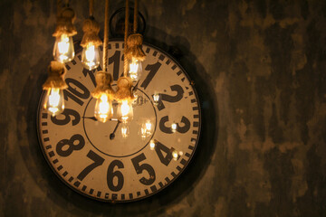 old clock hanging on the wall behind yellow bulbs