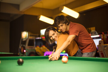 Young couple spending time in billiard room. Man teaching his girlfriend how to play pool.