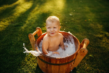 baby splashes in a basin in nature on a green tvava, at sunset. Good mood, child's smile, happiness from swimming in water, water splashes fly, good summer day
