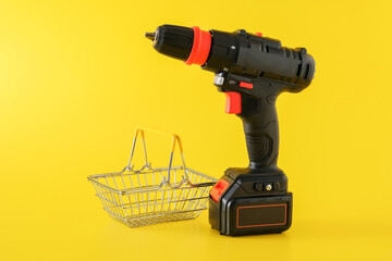 Modern black cordless screwdriver, drill with empty shopping basket on yellow background, copy space for text