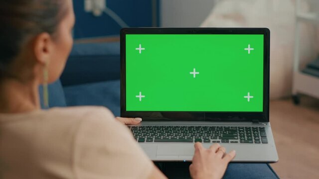 Close up of freelencer using laptop computer with mock up green screen chroma key display while sitting on sofa in living room., Woman working on personal business using isolated pc