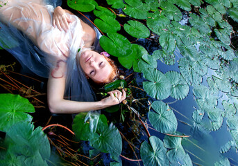 Young sexy unhappy crazy woman Lady Ophelia lies dying with rotten flowers, in white dress in the...