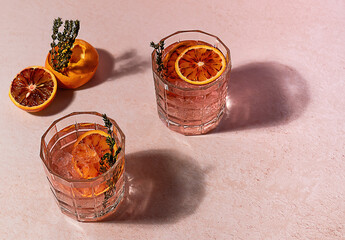 Pink gin cocktail with red blood orange and ice in sunny day. Trendy hard reflections.