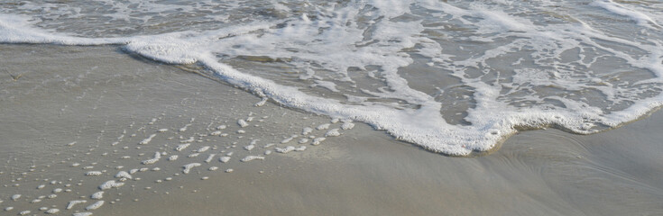 Mouvement de vagues formant de l'écume sur le sable fin d'une plage un jour ensoleillé, format bannière