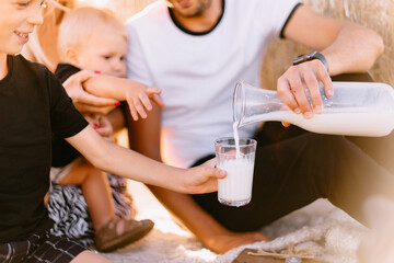 happy family had a picnic in the field near a haystack at sunset, mom dad and two sons drink milk eat croissants and fruits, the family is happy with smiles on their faces