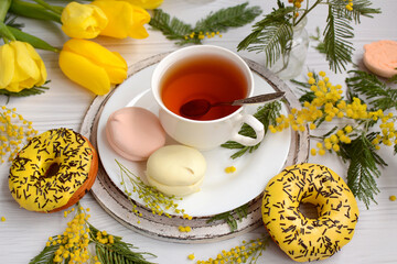 Top view of a spring composition of a cup of tea and marshmallows on a background of mimosa branches and yellow tulips. Closeup