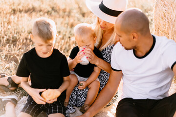happy family had a picnic in the field near a haystack at sunset, mom dad and two sons drink milk eat croissants and fruits, the family is happy with smiles on their faces